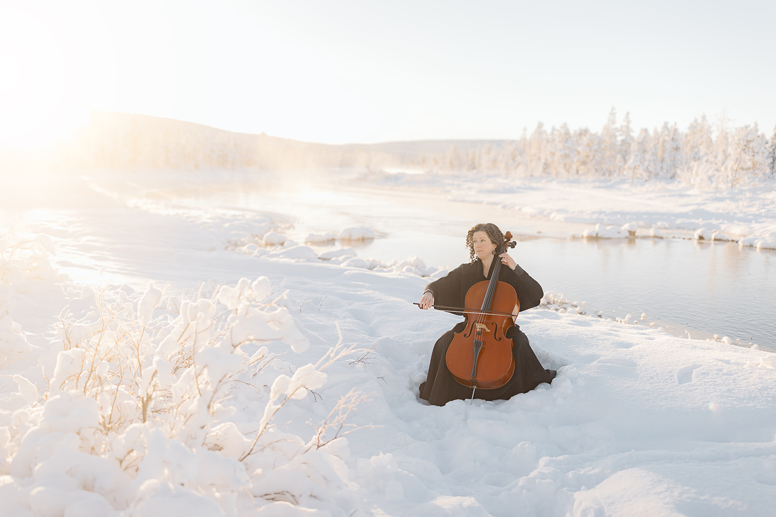 Musiker med cello i Jukkasjärvi, fotograferad i vinterljus med snötäckta träd och stilla natur.